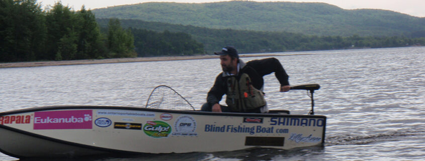 Person fishing on a small boat in a calm lake with hills in the background.