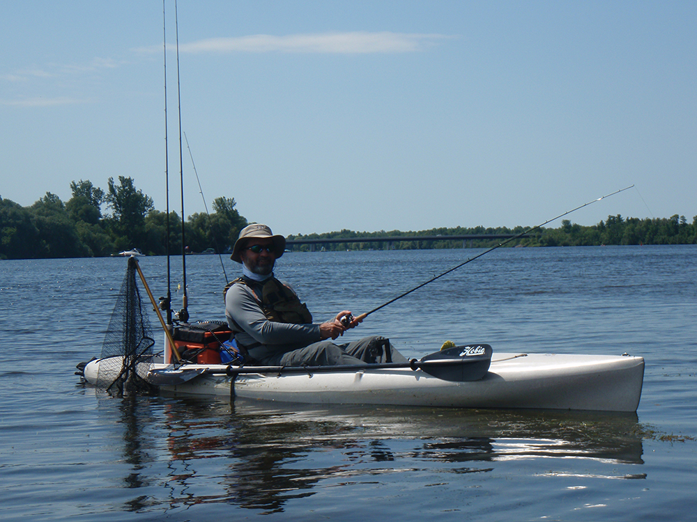 Person kayaking on a calm river under a clear sky.
