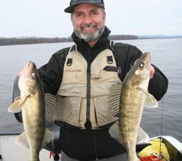 Man proudly holding two large fish on a boat.