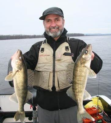 Man proudly holding two large fish on a boat.