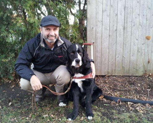 Man crouching with a black and white dog outside near a wooden fence.