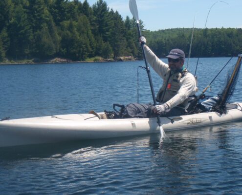 Person paddling a kayak on a calm lake surrounded by trees.