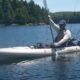 Person paddling a kayak on a calm lake surrounded by trees.