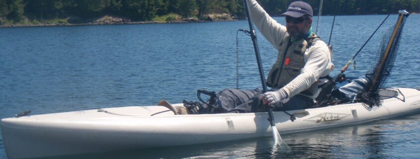 Person paddling a kayak on a calm lake surrounded by trees.