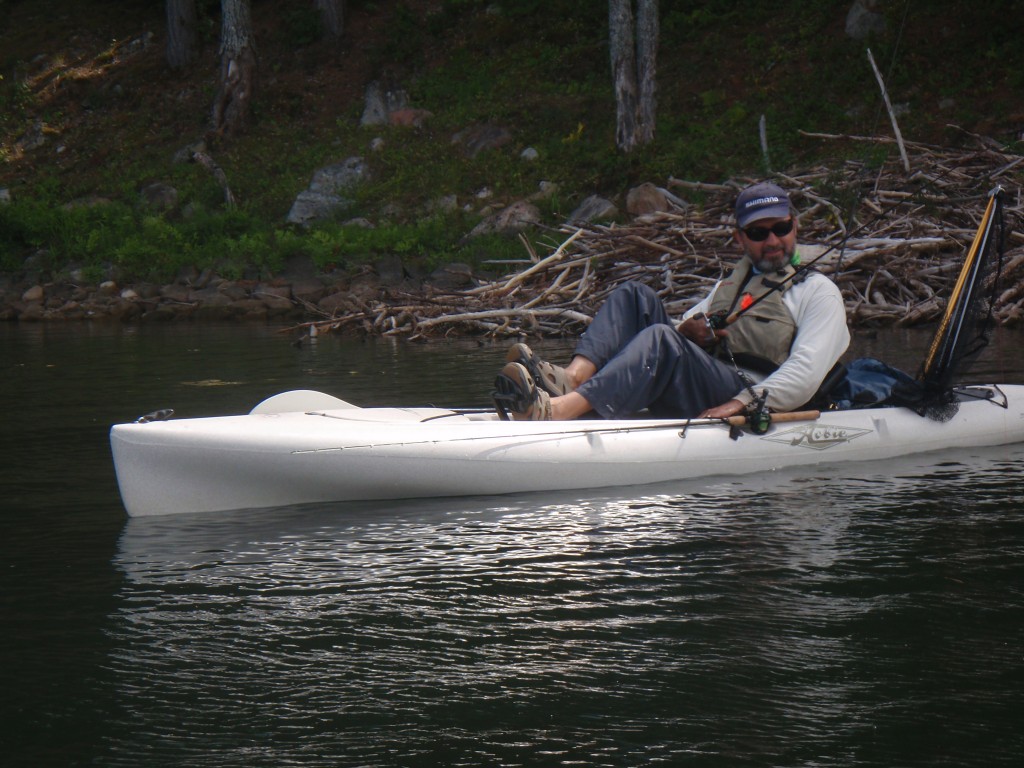 A person relaxing on a kayak in calm water near a rocky shore.