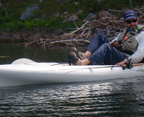 A person fishing while lying on an inflatable kayak in calm water.