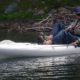 A person fishing while lying on an inflatable kayak in calm water.