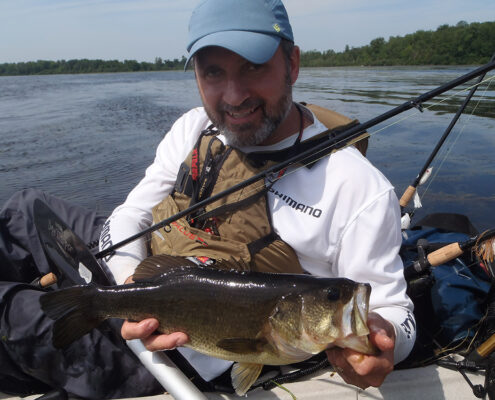 Man holding a large fish by the water.