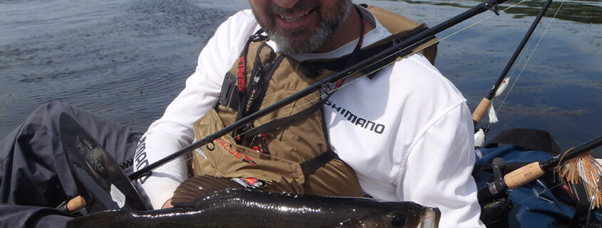 Man holding a large fish by the water.