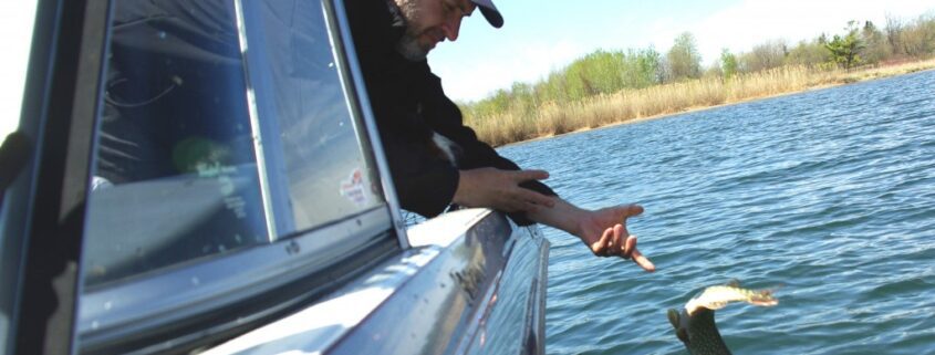 Man reaching out from boat to touch water with paddle.