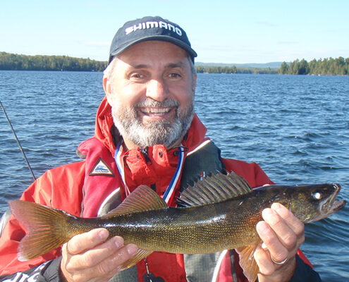 Man proudly holding a freshly caught fish near a lake.