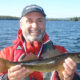 Man proudly holding a freshly caught fish near a lake.