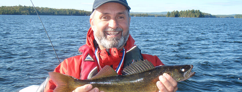 Man proudly holding a freshly caught fish near a lake.