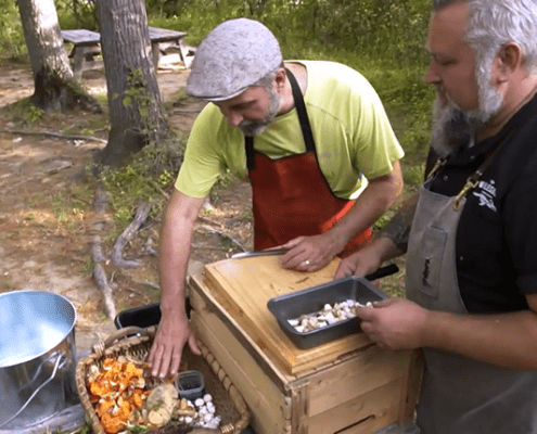 Two men preparing food outdoors in forest.