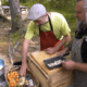 Two men preparing food outdoors in forest.