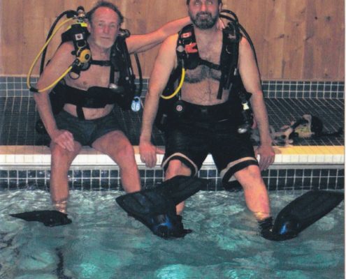 Two scuba divers sitting by the pool.